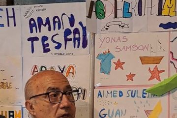 Vito Fiorino mostra il simbolo di carta ricavato tagliando una barchetta, alle sue spalle i disegni dei ragazzi con i nomi delle vittime del 3 ottobre 2013