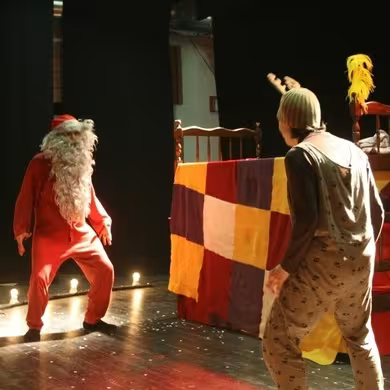 scena con attore travestito da Babbo Natale e un grande letto e un altro attore travestito da personaggio di fantasia con cappellino da renna